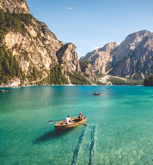 Projects Aerial view of a small boat anchored in clear turquoise coastal waters near rocky cliffs.