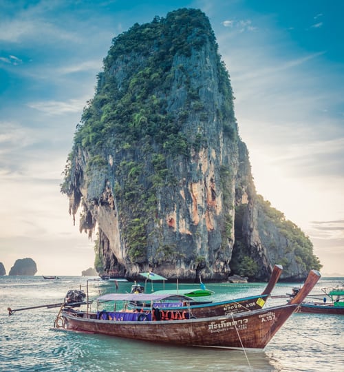 Projects Traditional wooden boat floating near a giant rock island in the sea.