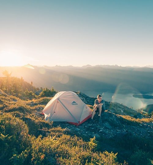Projects * : "A small white camping tent set up on a grassy hill overlooking a foggy valley at dusk."