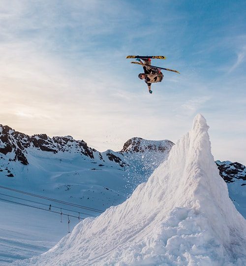 Projects : "A skier performing a mid-air jump twist over a snowy ridge against a clear blue sky."